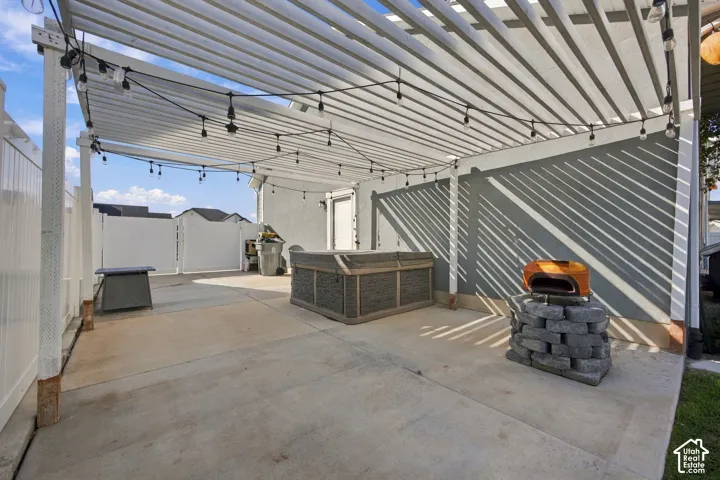 Paved patio area featuring a slatted pergola, string lighting, and stucco exterior walls