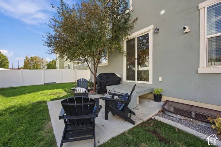 Private backyard with a concrete patio, mature tree, white privacy fence, and sliding glass door access