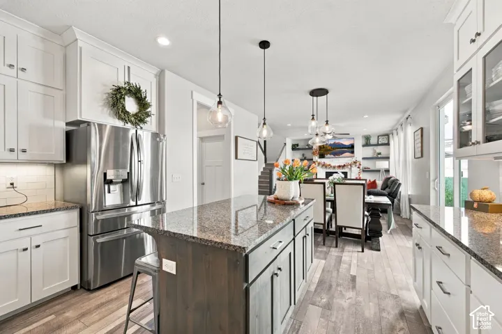 Kitchen featuring white cabinetry, granite countertops, stainless steel refrigerator, and wood-finish flooring