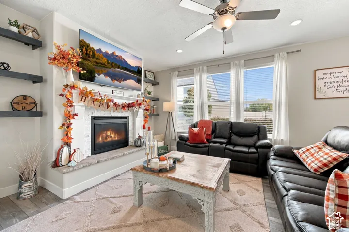 Living area featuring a white brick fireplace with a stone hearth, built-in shelving, multiple windows, and a ceiling fan with integrated lighting