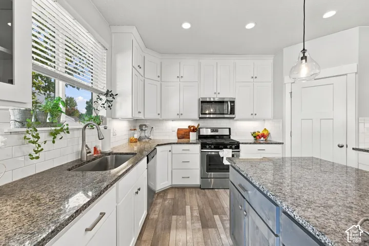 White cabinetry, stainless steel appliances, wood-finish flooring, undermount sink, and durable countertops