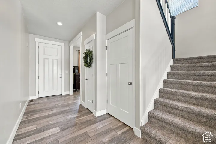 Wood-finish flooring, white panel doors, recessed lighting, carpeted stairs, and a dark-finished stair railing