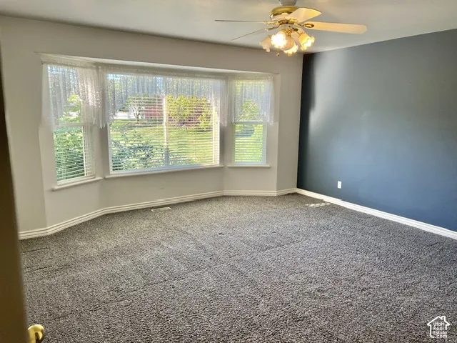 Bay window with multiple panes, ceiling fan light fixture, wall-to-wall carpeting, and painted walls