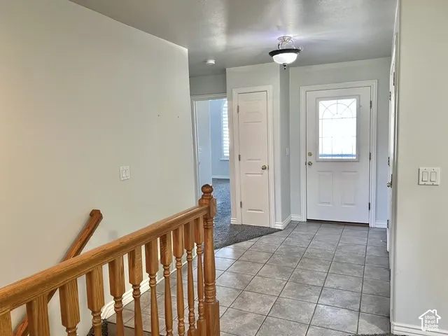 Foyer featuring tile flooring, a solid wood staircase with balusters, a white entry door with decorative glass, and a flush-mount ceiling light fixture