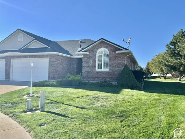 Brick facade with white trim, arched window with interior shutters, asphalt shingle roof, and attached garage