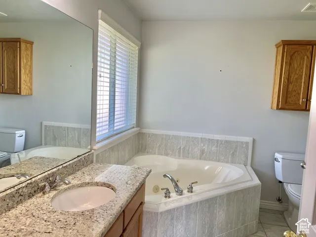 Built-in soaking tub with tile surround, vanity with stone countertop and integrated sink, and window with blinds