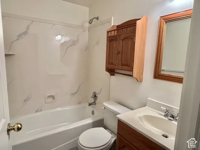 White bathtub with a patterned surround, chrome shower fixtures, wood-finish vanity with an integrated sink, and a framed mirror