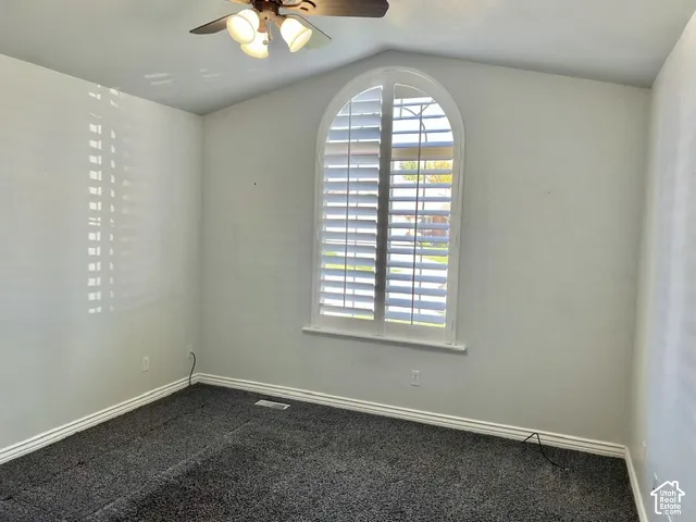 Vaulted ceiling featuring a ceiling fan with integrated lighting, arched window with plantation shutters, and gray carpeting