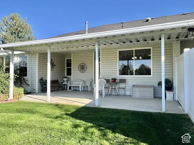 Expansive covered patio with concrete flooring, supported by multiple white posts, featuring an exterior wall with horizontal siding and multiple windows
