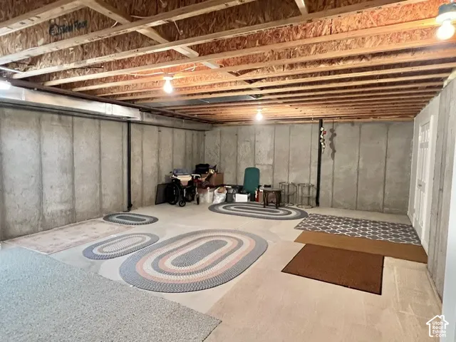 Spacious unfinished basement with exposed wooden beam ceiling, recessed lighting, and concrete walls