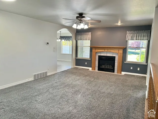Carpeted living area featuring a fireplace with a wood mantle and tile surround, two windows, and an arched doorway