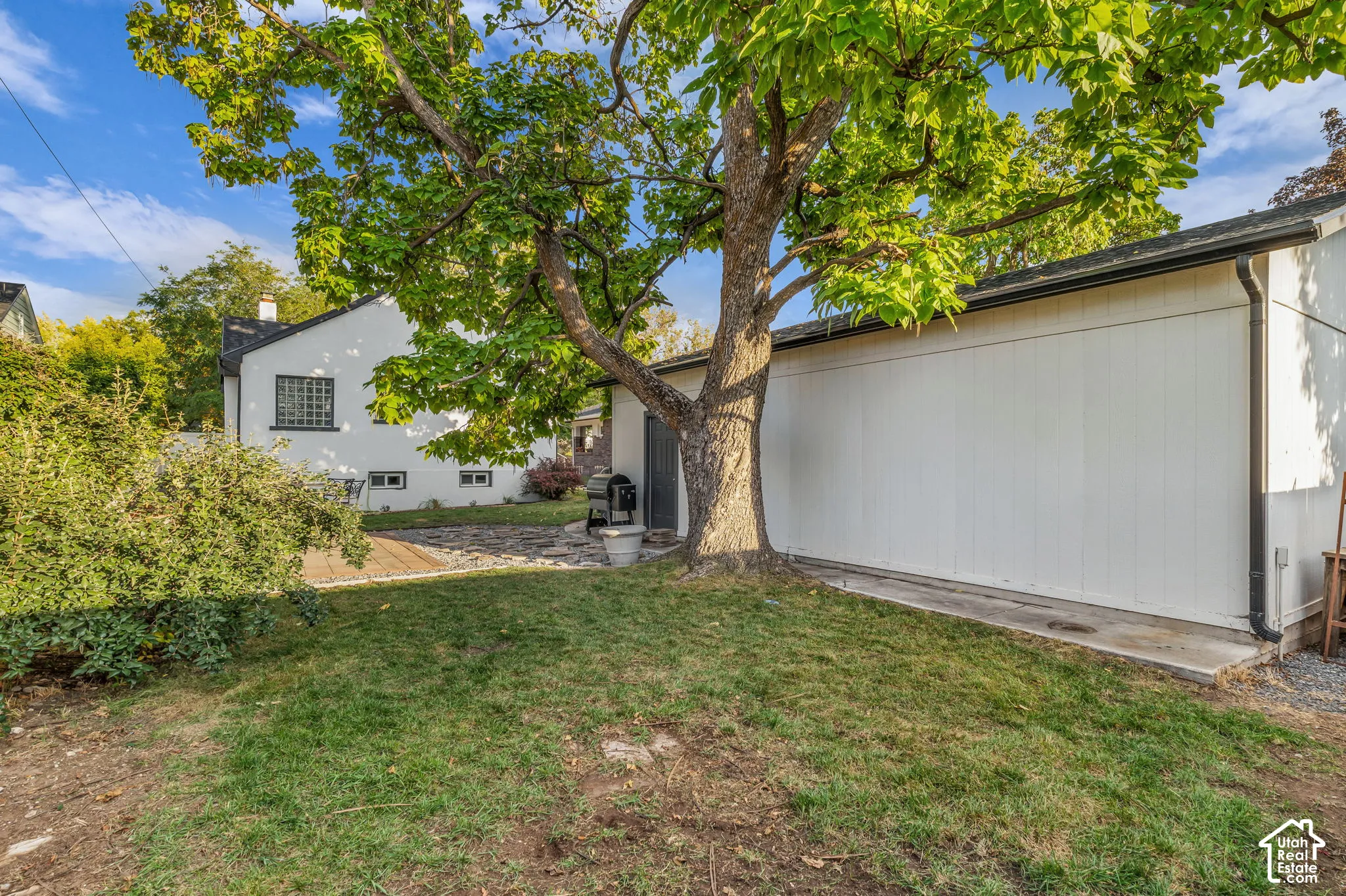 Expansive lawn area with a mature tree, white stucco exterior, glass block window, and black gutters