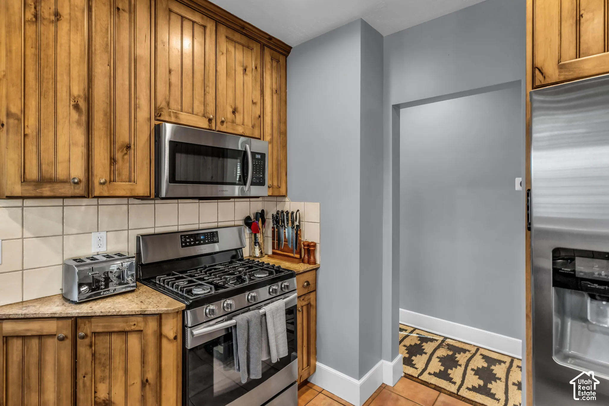 Kitchen featuring wood cabinetry, stainless steel microwave, gas range, and stone-finish countertops