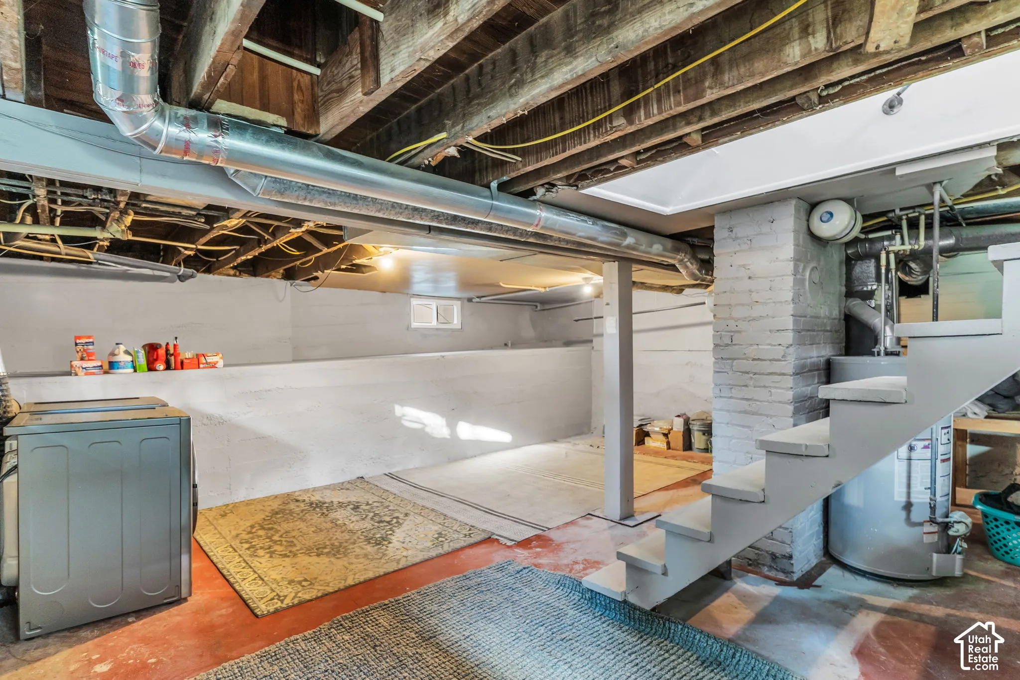 Exposed ceiling joists and ductwork, painted concrete walls, painted brick column, and a fixed staircase