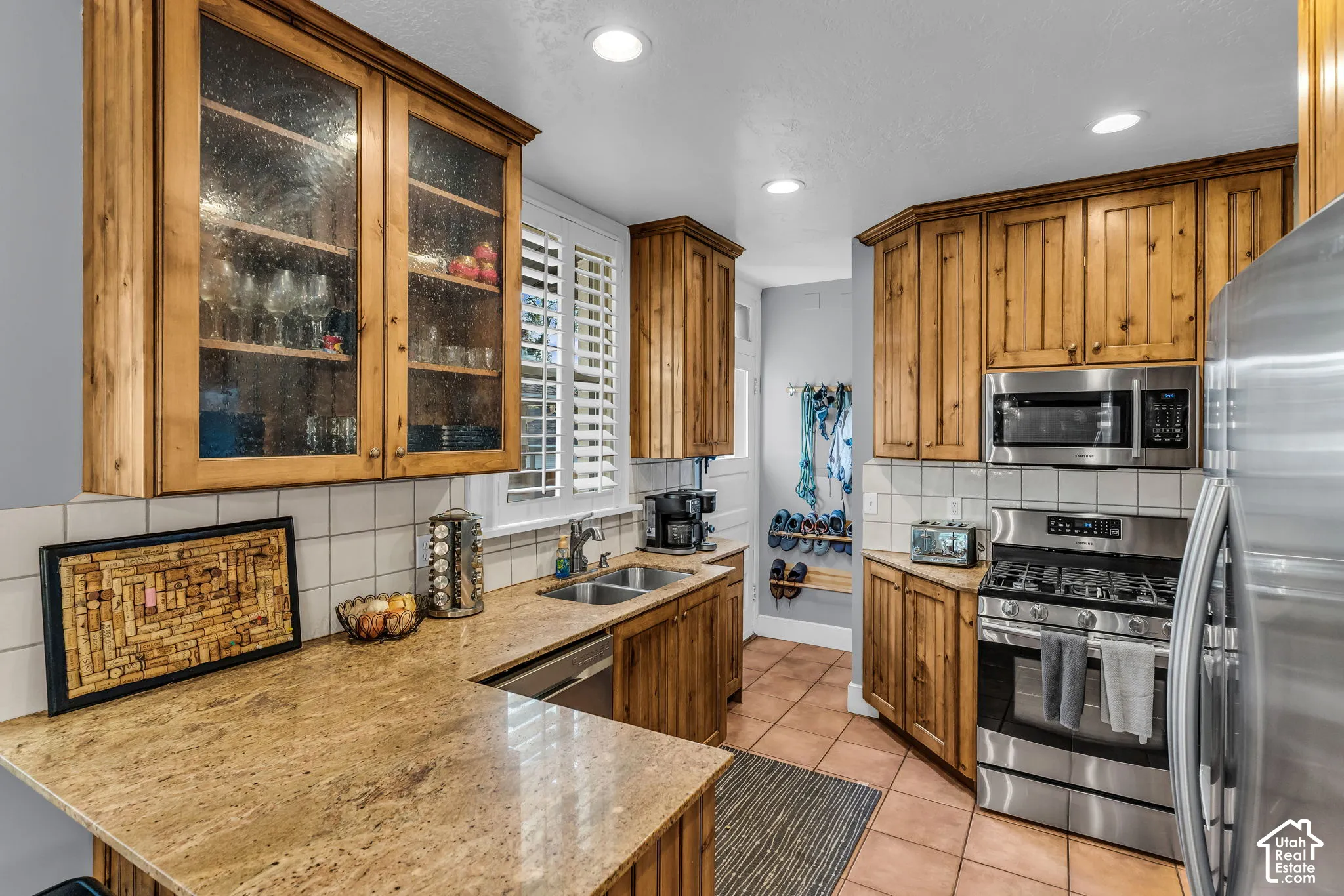 Kitchen featuring natural wood cabinetry, light-colored tile backsplash, granite countertops, and stainless steel appliances
