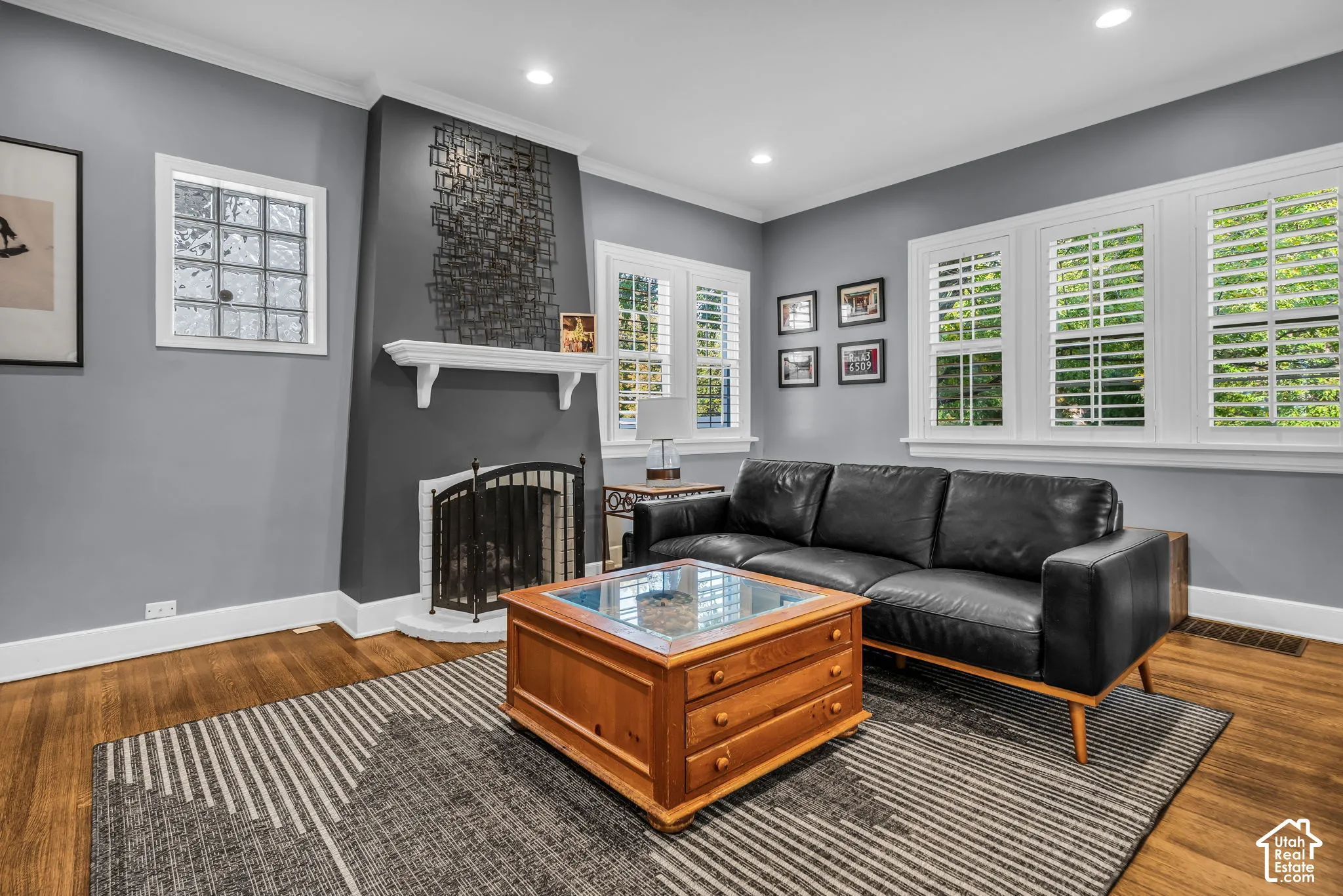 Recessed lighting, wood-finish flooring, white crown molding, glass block window, and a built-in fireplace with a white mantel and screen