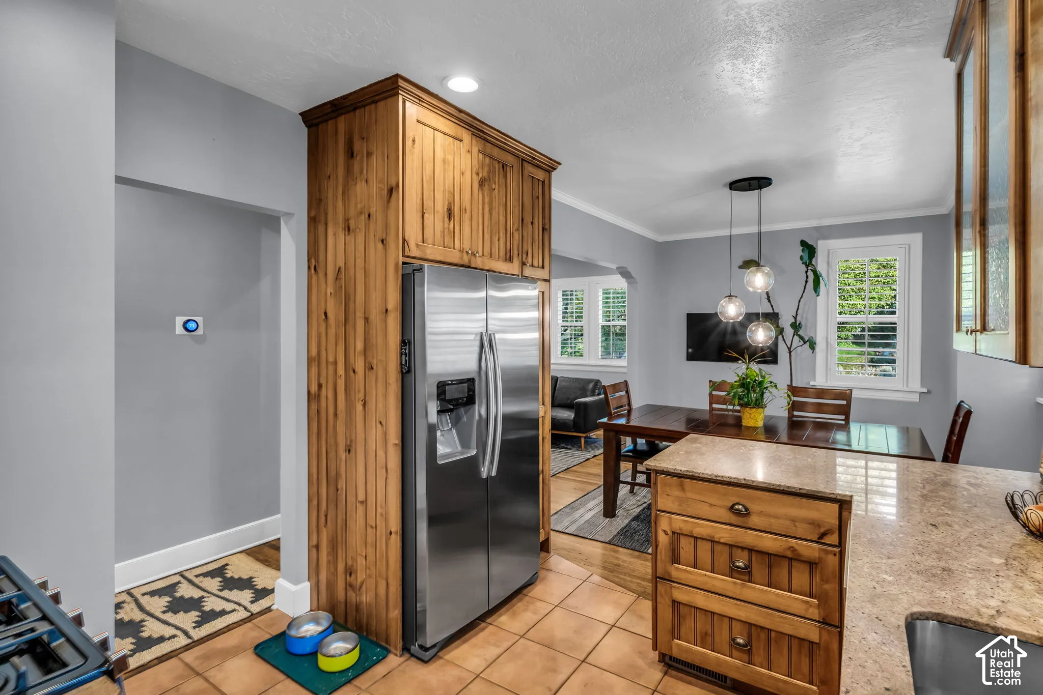Stainless steel refrigerator, custom wood cabinetry, tiled flooring, pendant lighting, and granite-style countertops