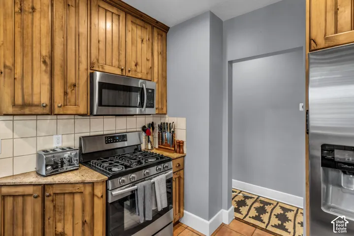 Kitchen featuring wood cabinetry, stainless steel microwave, gas range, and stone-finish countertops