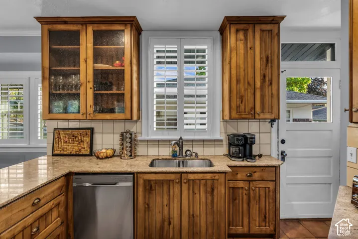 Wood-finish cabinetry with glass-front uppers, stainless steel dishwasher, integrated sink, and plantation shutters