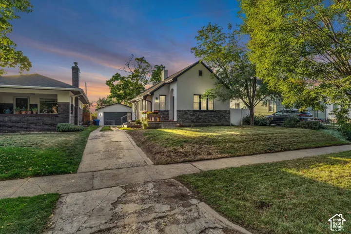 Stucco and stone exterior, detached garage, concrete driveway, and established trees