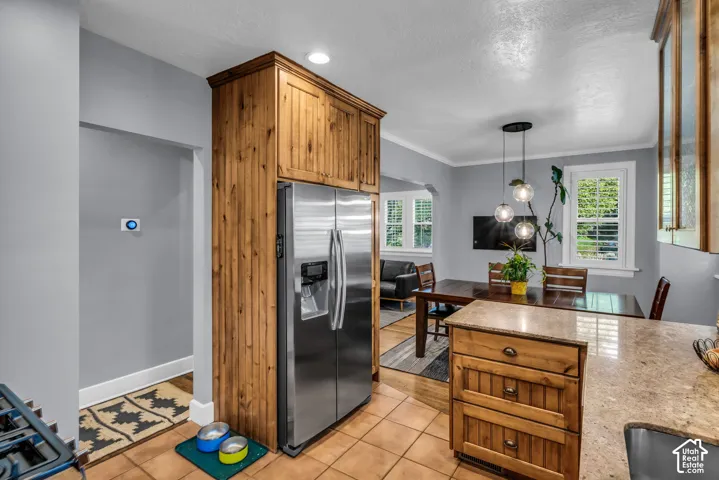 Stainless steel refrigerator, custom wood cabinetry, tiled flooring, pendant lighting, and granite-style countertops