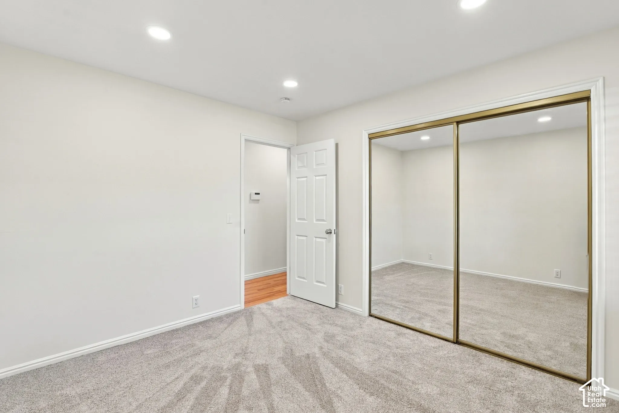 Recessed ceiling lighting, white interior walls, light gray carpet flooring, white interior door, and mirrored sliding closet doors
