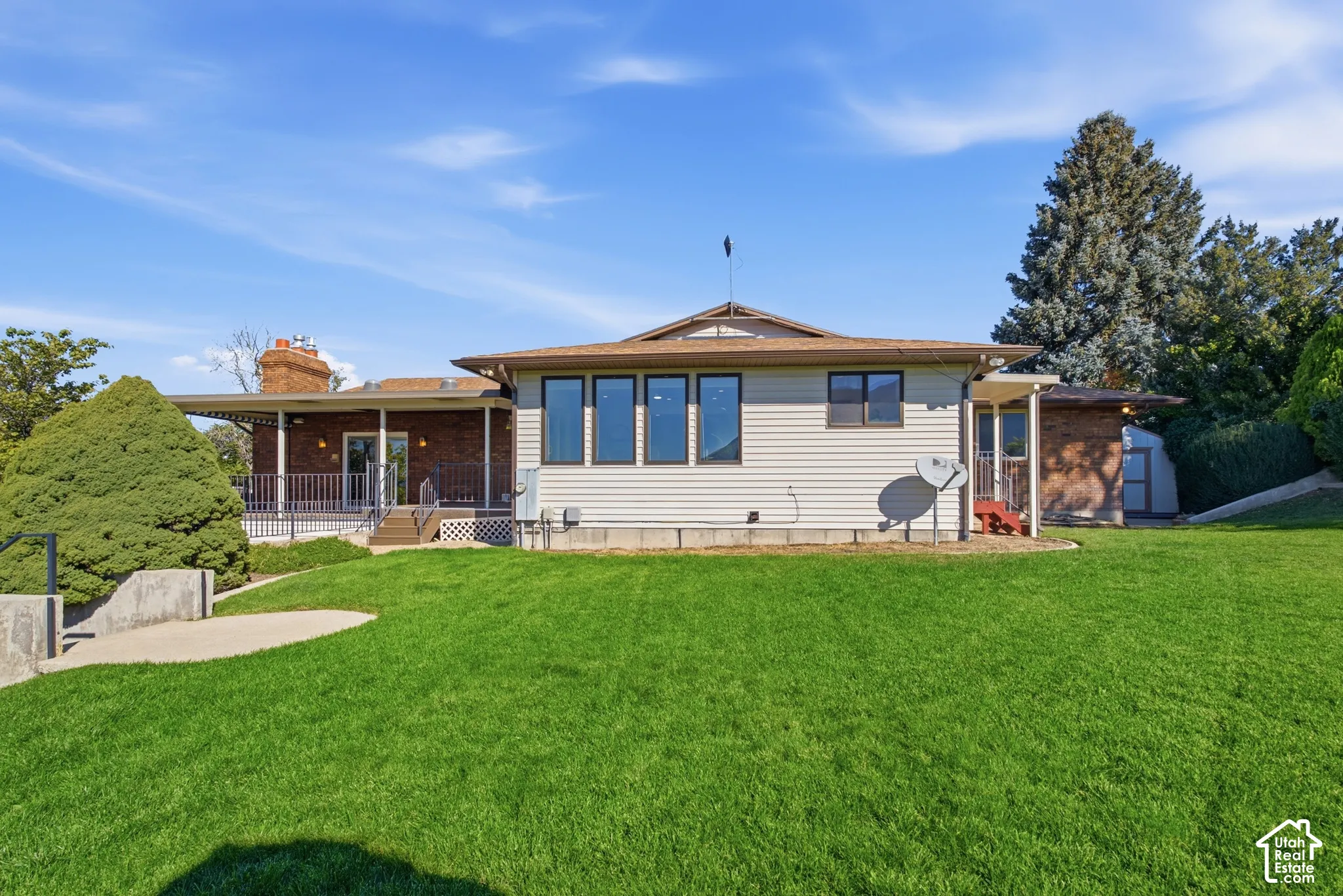 Expansive green lawn, brick exterior accents, large windows, covered patio with railing, and mature landscaping