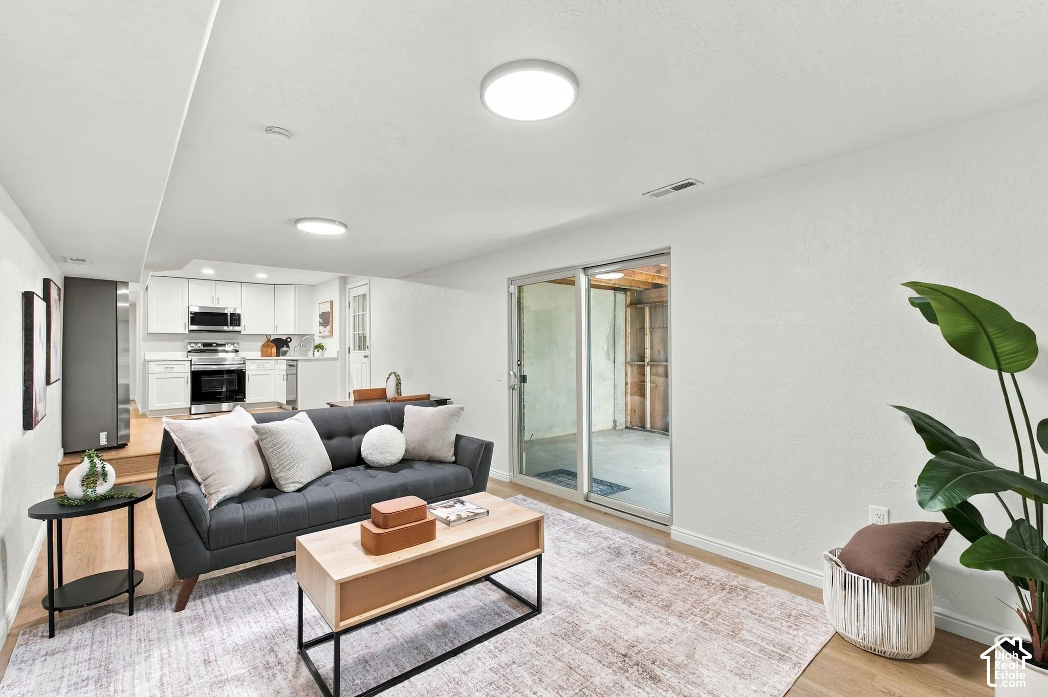 Open-concept living area featuring wood-finish flooring, recessed lighting, and a full kitchen with stainless steel appliances and white cabinetry