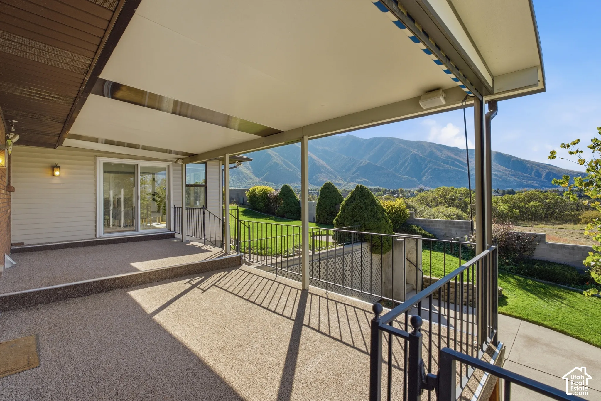 Expansive covered patio with retractable shade system and metal railing, overlooking manicured lawn and mature landscaping