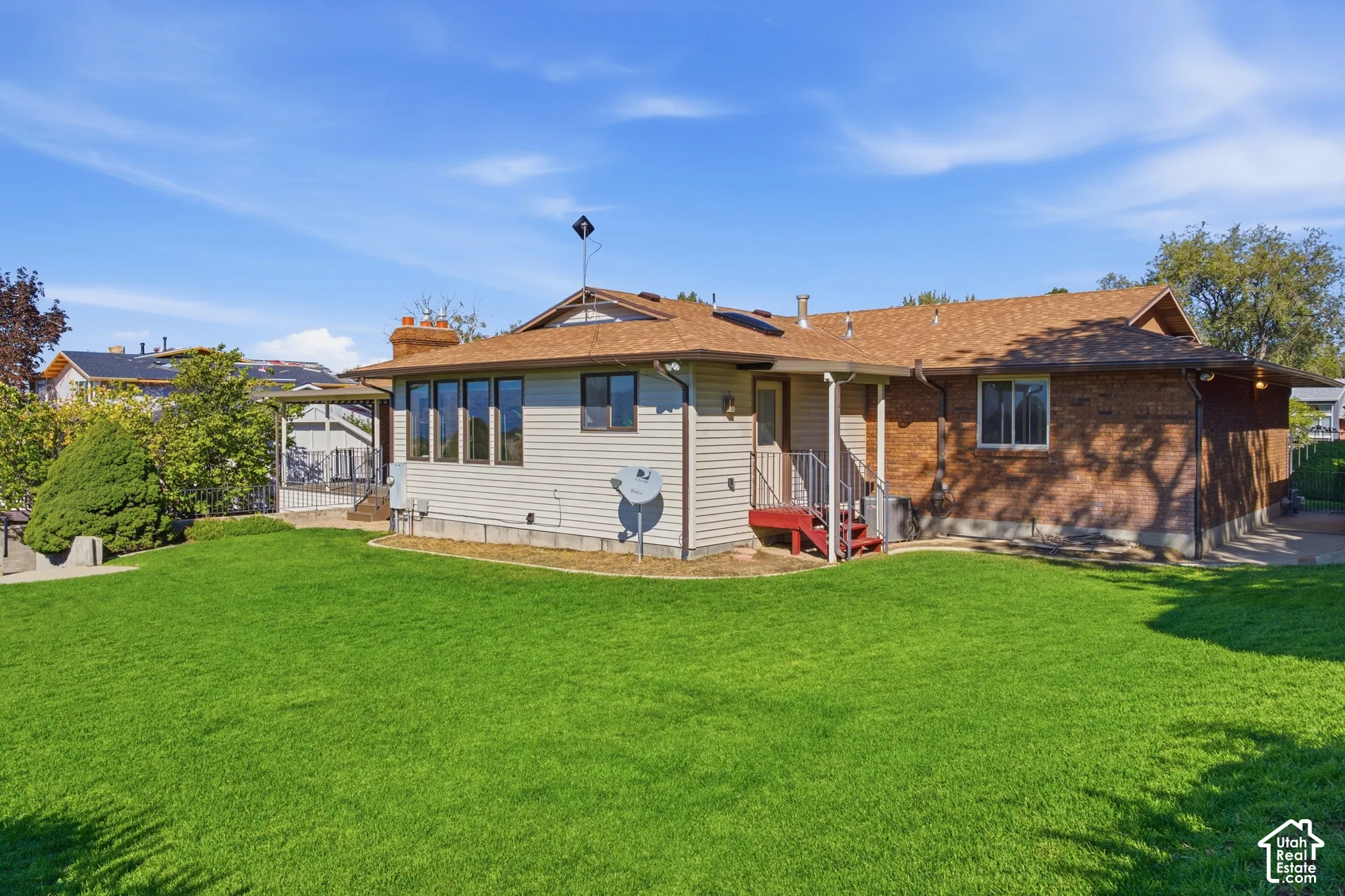 Expansive green lawn with a multi-level structure featuring a brick exterior and horizontal siding