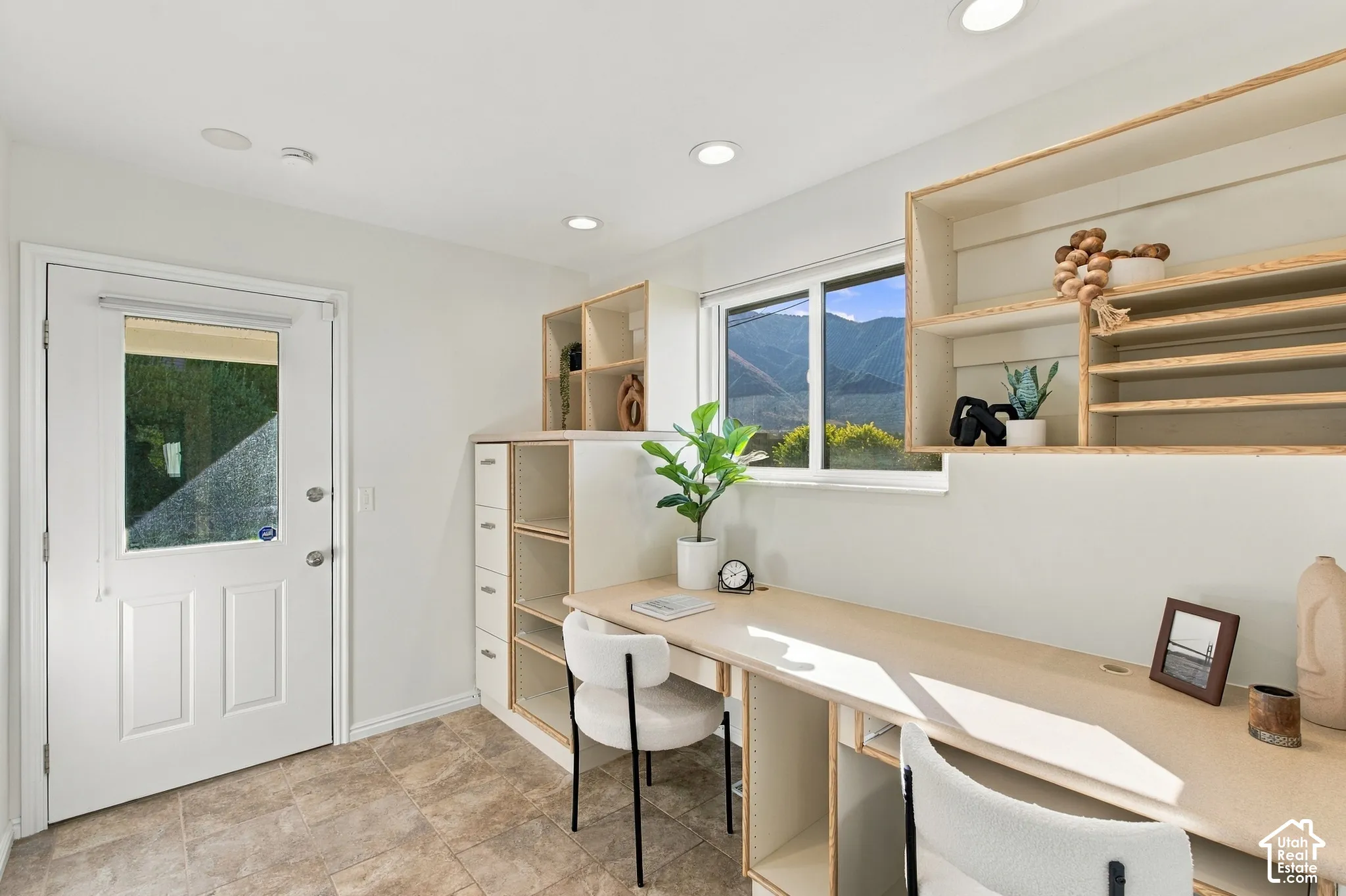 Recessed lighting, light wood-finish built-in desk, built-in shelving, white paneled door with glass insert, and tiled flooring