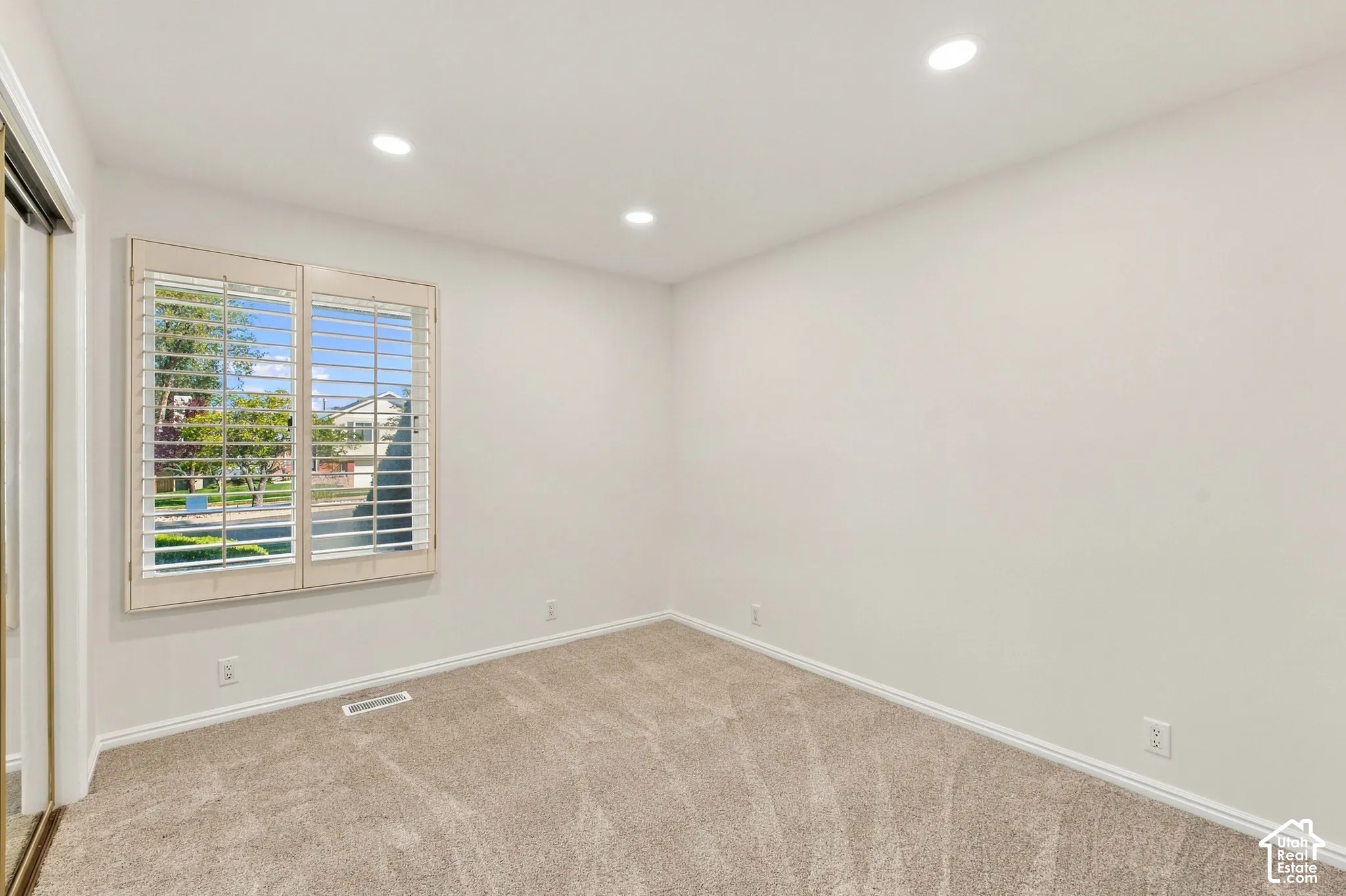 Recessed lighting, light neutral-toned walls, wood-framed window with plantation shutters, neutral-toned carpet flooring, and white trim