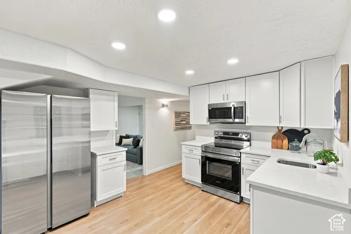 Kitchen featuring white cabinetry, stainless steel appliances, light-toned wood-finish flooring, recessed lighting, and light-colored countertops
