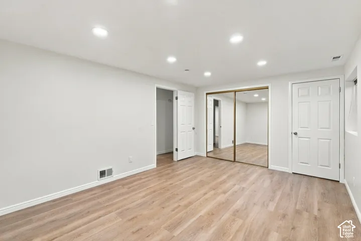 Recessed lighting, wood-finish flooring, white walls, white doors, and mirrored closet doors