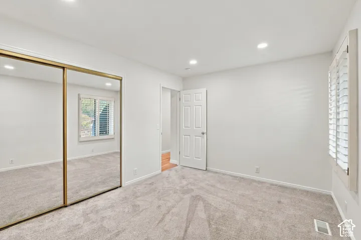 Recessed lighting, mirrored closet doors, plantation shutters, and light-toned carpeting with white walls