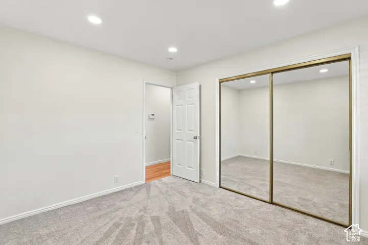 Recessed ceiling lighting, white interior walls, light gray carpet flooring, white interior door, and mirrored sliding closet doors