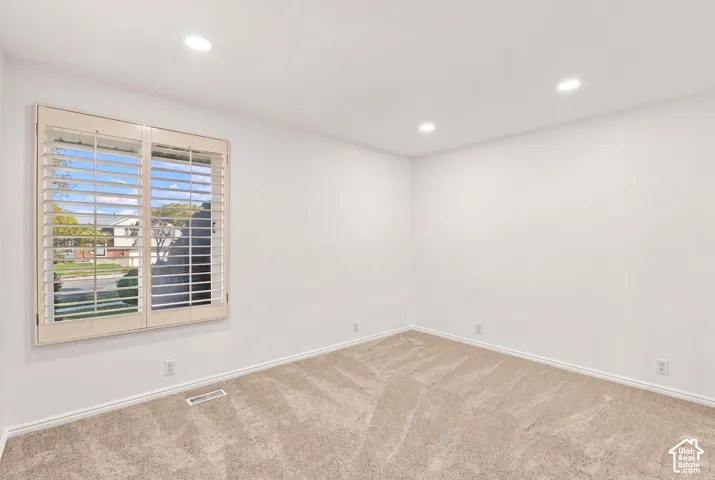 Recessed lighting illuminates the room with neutral carpeting and a window featuring plantation shutters