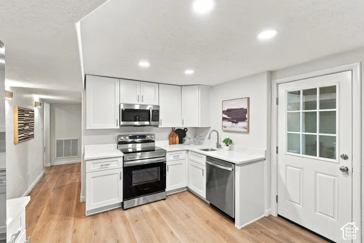 Kitchen featuring white cabinetry, stainless steel appliances, light-toned countertops, wood-finish flooring, and recessed lighting