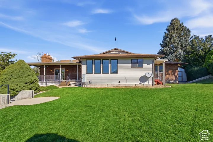 Expansive green lawn, brick exterior accents, large windows, covered patio with railing, and mature landscaping