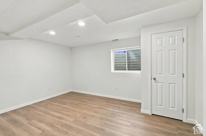 Recessed lighting, wood-finish flooring, white paneled door, and a single window