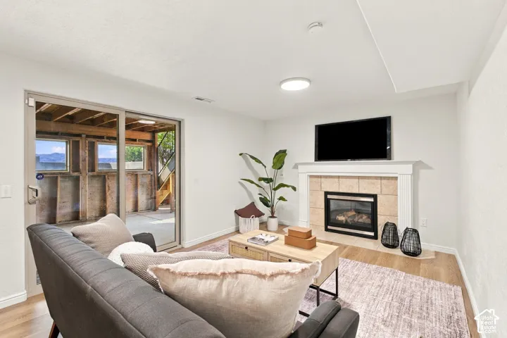 Living area featuring a gas fireplace with a tiled surround and white mantel, wood-finish flooring, and a sliding glass door