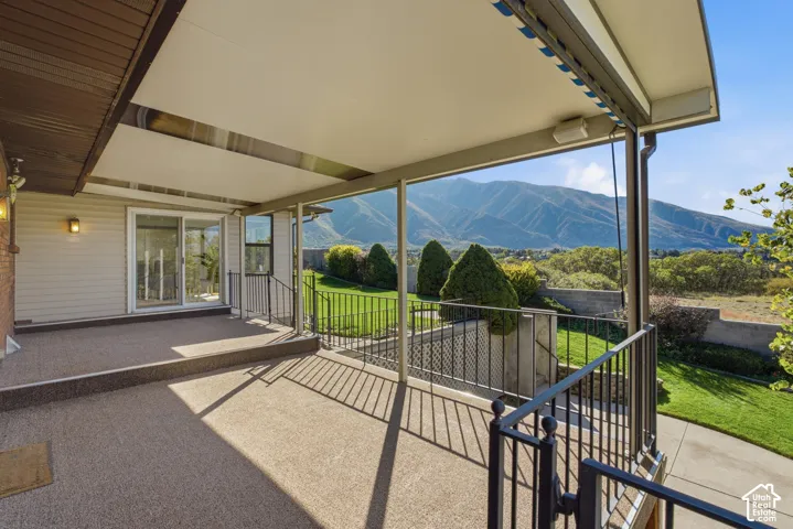 Expansive covered patio with retractable shade system and metal railing, overlooking manicured lawn and mature landscaping