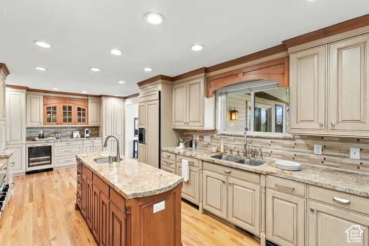 Kitchen featuring wood-finish flooring, recessed lighting, a central island with a sink, light-toned cabinetry, and granite countertops