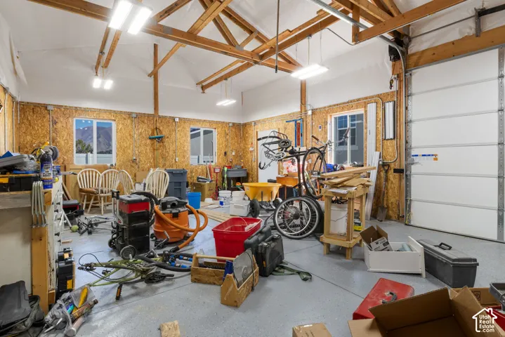 Spacious garage with exposed beam ceiling, multiple windows, overhead lighting, and a large garage door