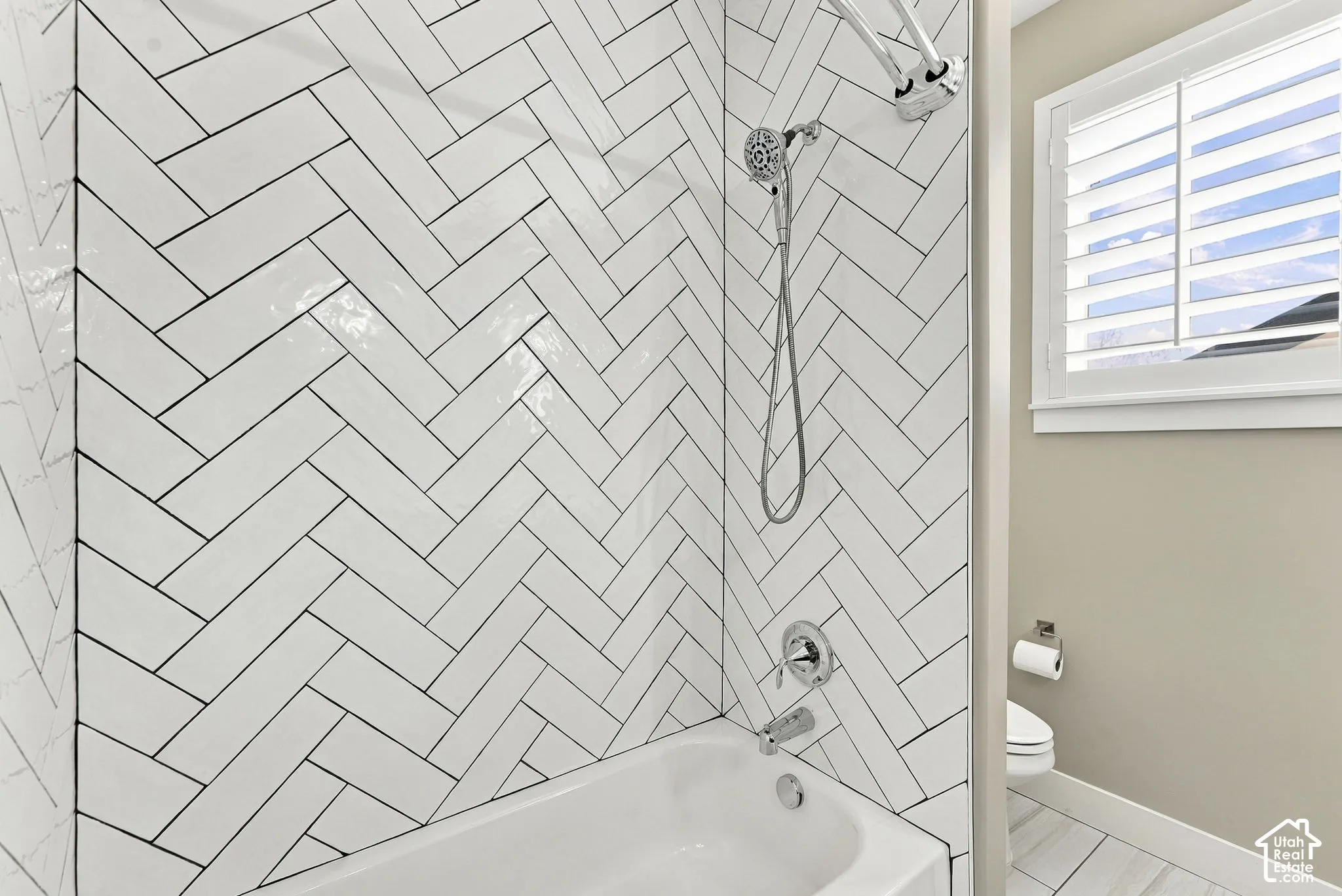 Herringbone tile shower surround with dual shower heads, white bathtub, white window shutters, and light-toned wall paint