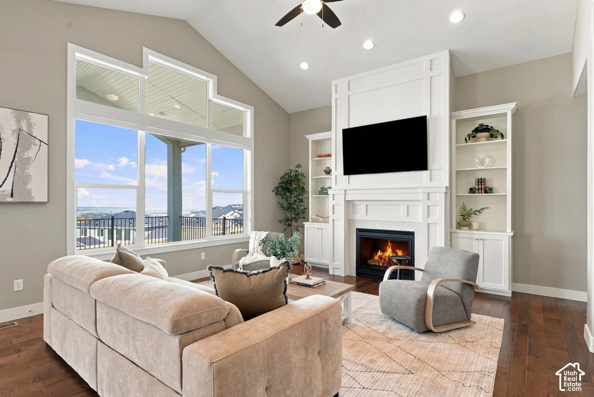 Vaulted ceiling with a ceiling fan, a fireplace with built-in shelving, expansive windows, and wood-finish flooring