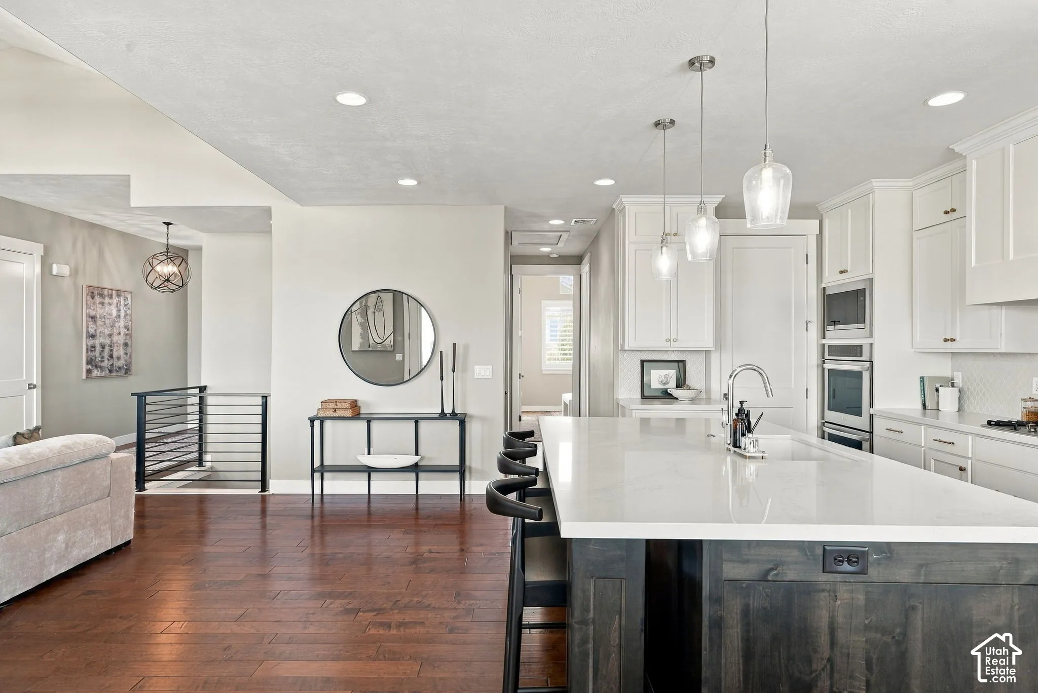 Open-concept kitchen featuring an oversized island with seating, pendant lighting, white cabinetry, and stainless steel built-in appliances