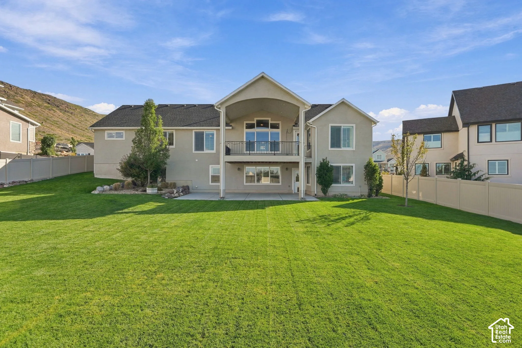 Expansive backyard featuring a manicured lawn, an upper-level balcony with a black railing, and a lower-level covered patio