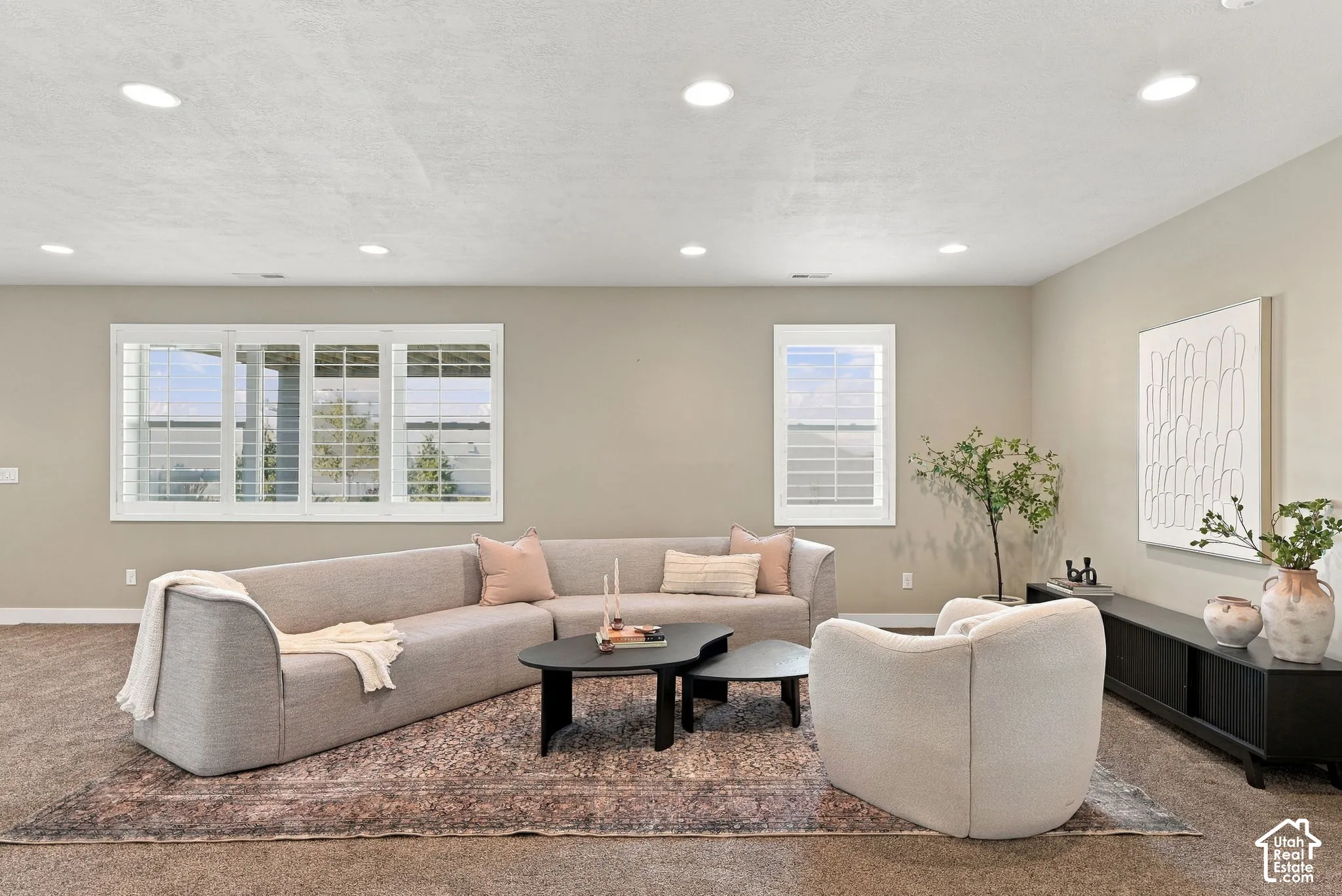 Basement living room area, recessed lighting, large windows with plantation shutters, neutral wall tones, and carpet flooring