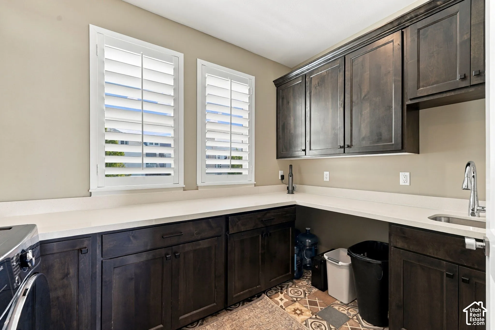 Dark wood-finish cabinetry, white plantation shutters, white countertops, built-in sink, and patterned floor tile